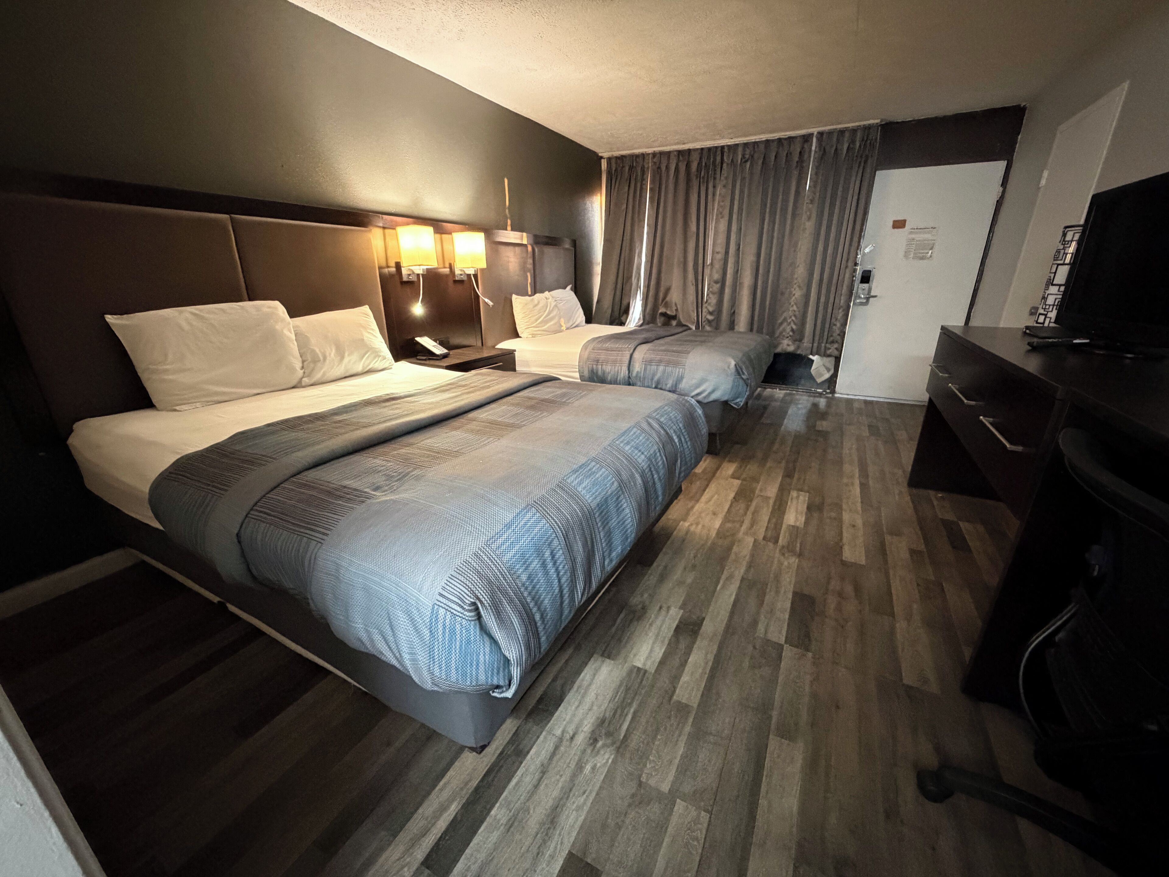 A hotel room with two beds, a desk, a chair, and a television.