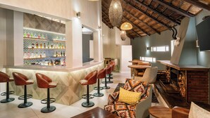 Una zona de bar con taburetes, una barra con botellas y un área de estar con un sofá estampado y mesas de madera.