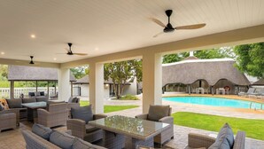 Un patio al aire libre con mobiliario de mimbre, ventiladores de techo y vistas a una piscina.