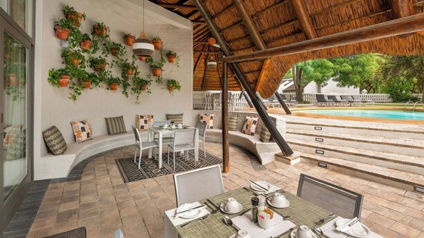 Un área de comedor con una mesa preparada para dos personas, un banco de asientos y una piscina al fondo.