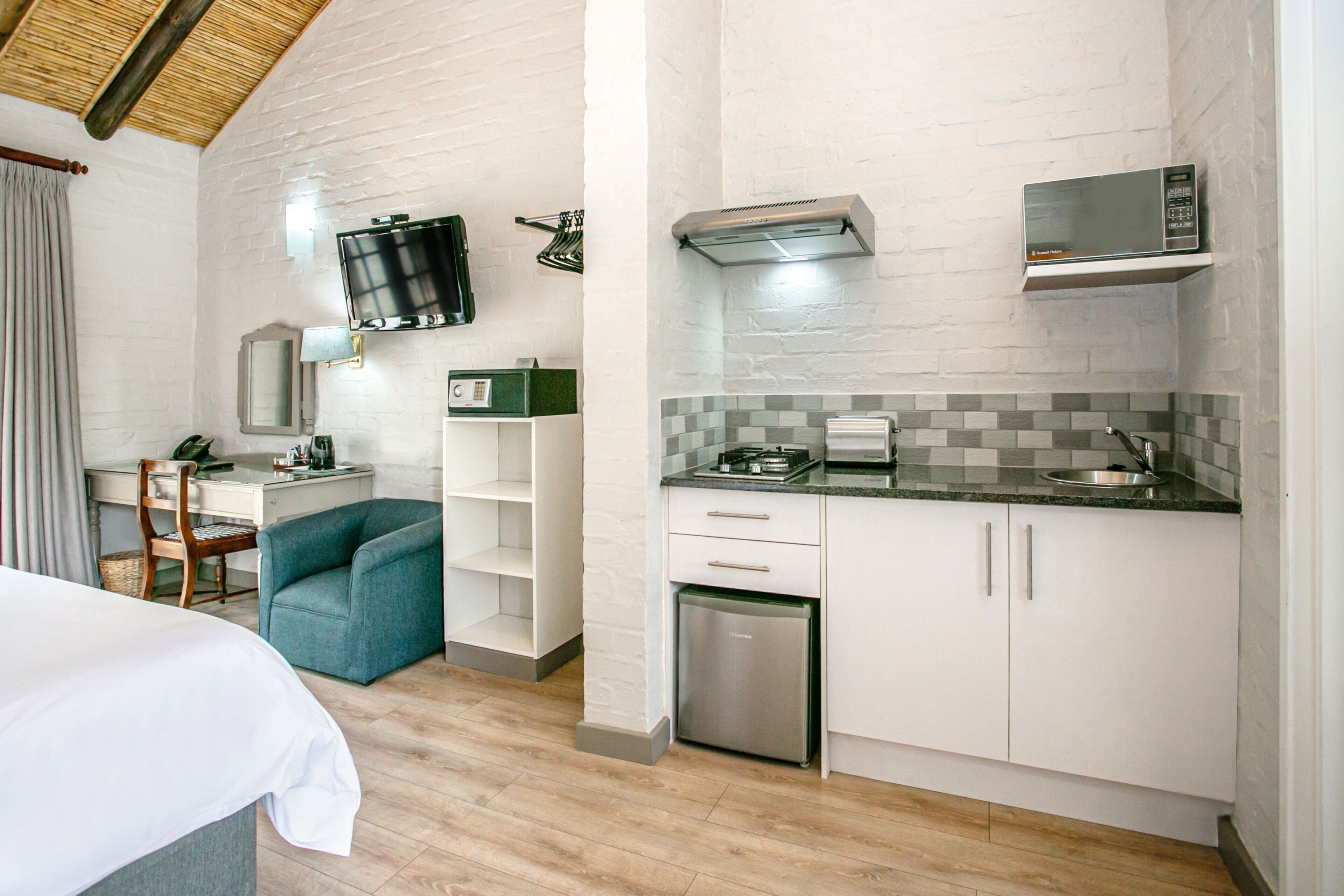 A compact hotel room with a kitchenette, a bed, a desk with a chair, and a television mounted on the wall.