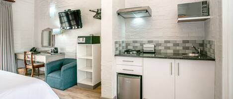 Une chambre d’hôtel compacte comprenant un coin cuisine, un lit, un bureau avec une chaise et un téléviseur fixé au mur.