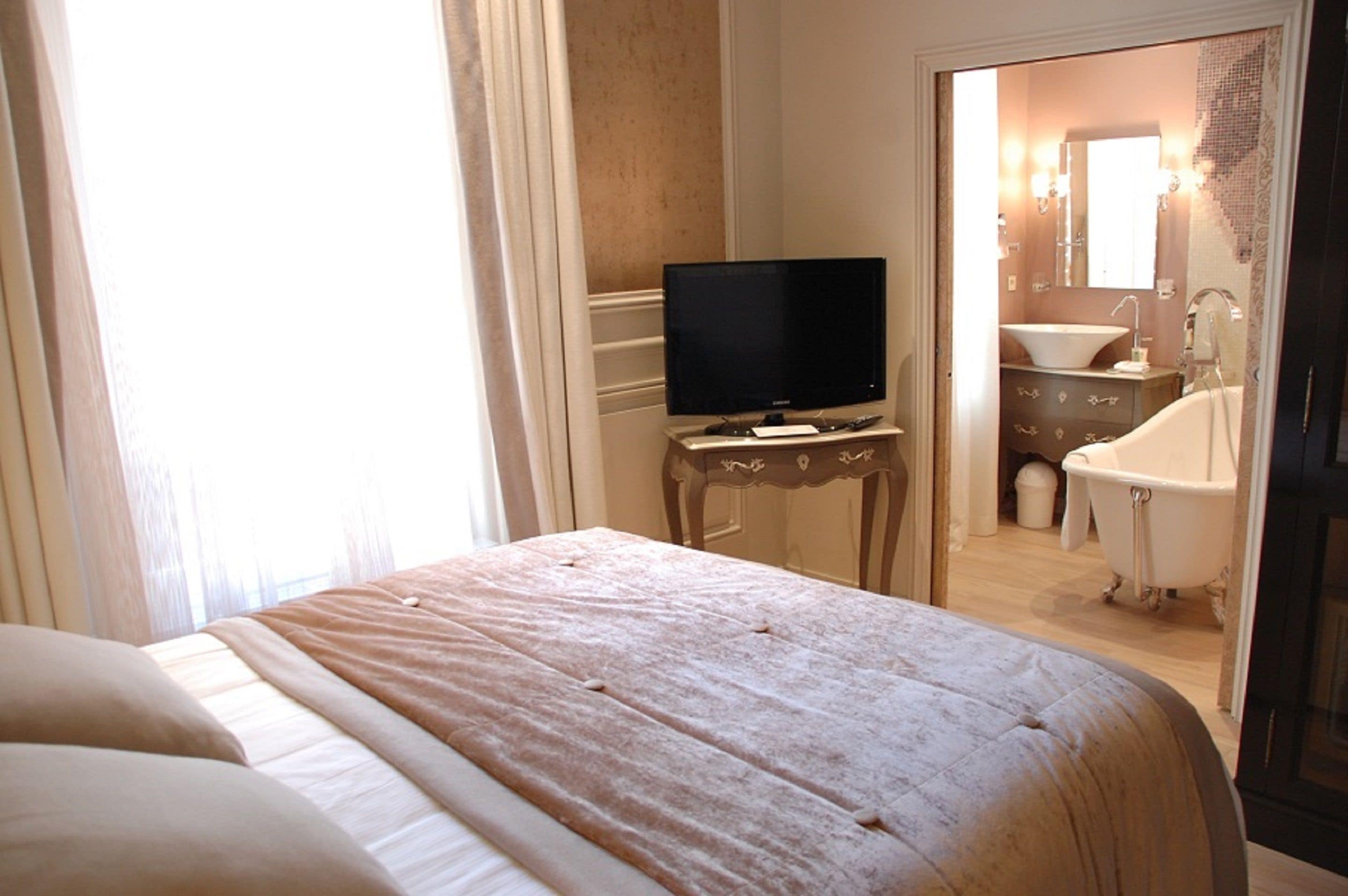 Habitación de hotel con cama, televisor sobre una mesita, baño con bañera y lavamanos.