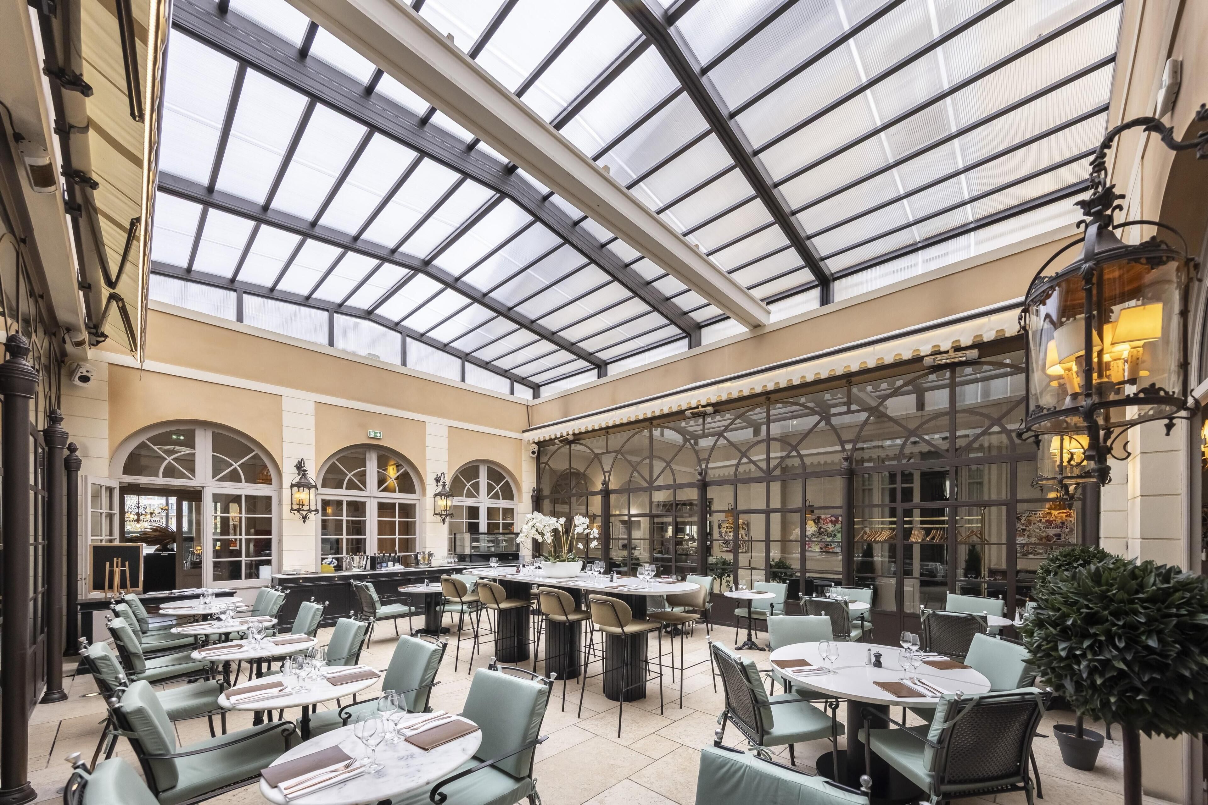 A spacious indoor dining area with a glass ceiling, multiple tables, and chairs.