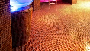 A modern spa area with a large heated floor, a glass-enclosed hot tub, and a red textured wall.