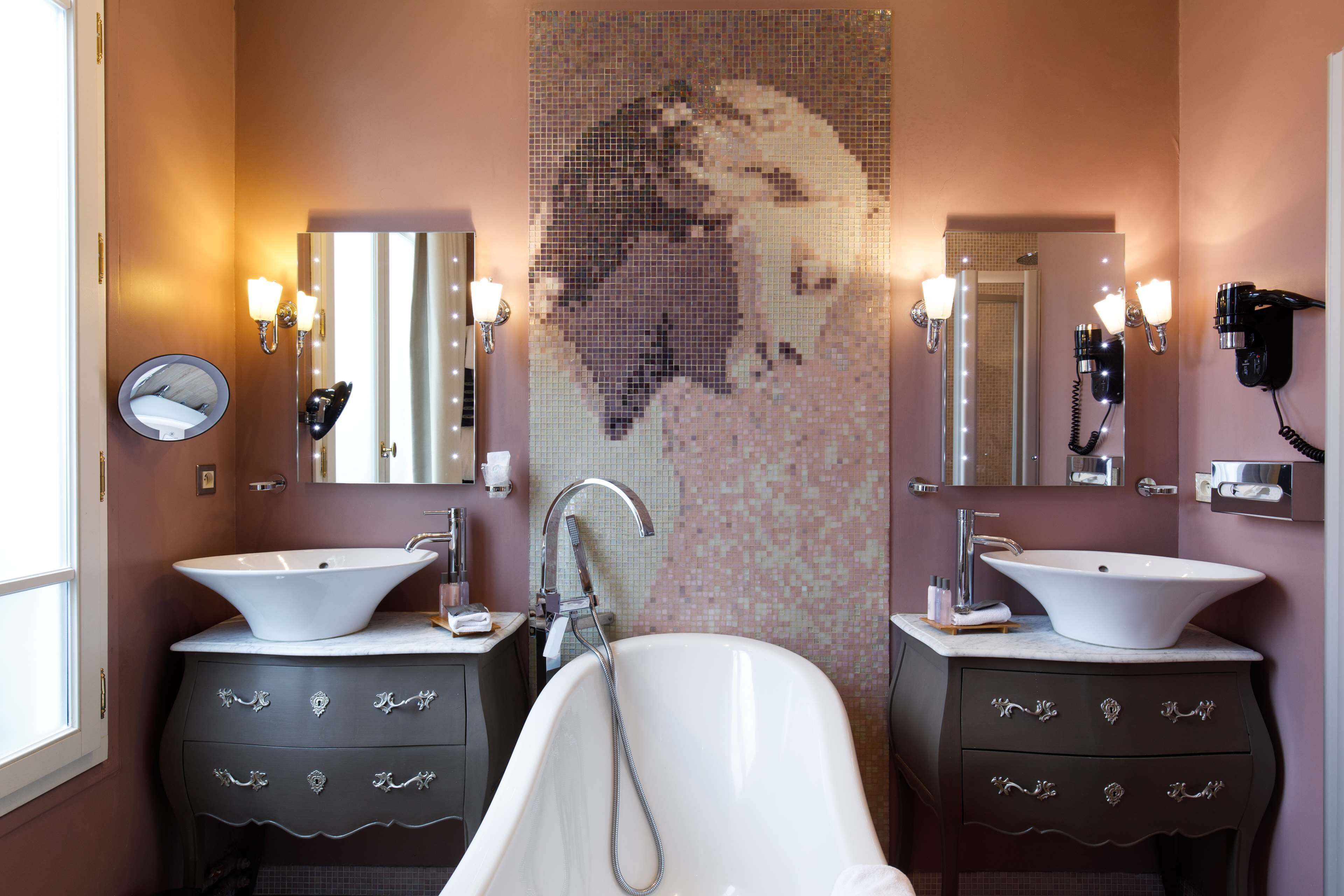 A bathroom with two sinks, a large bathtub, and a mosaic wall.
