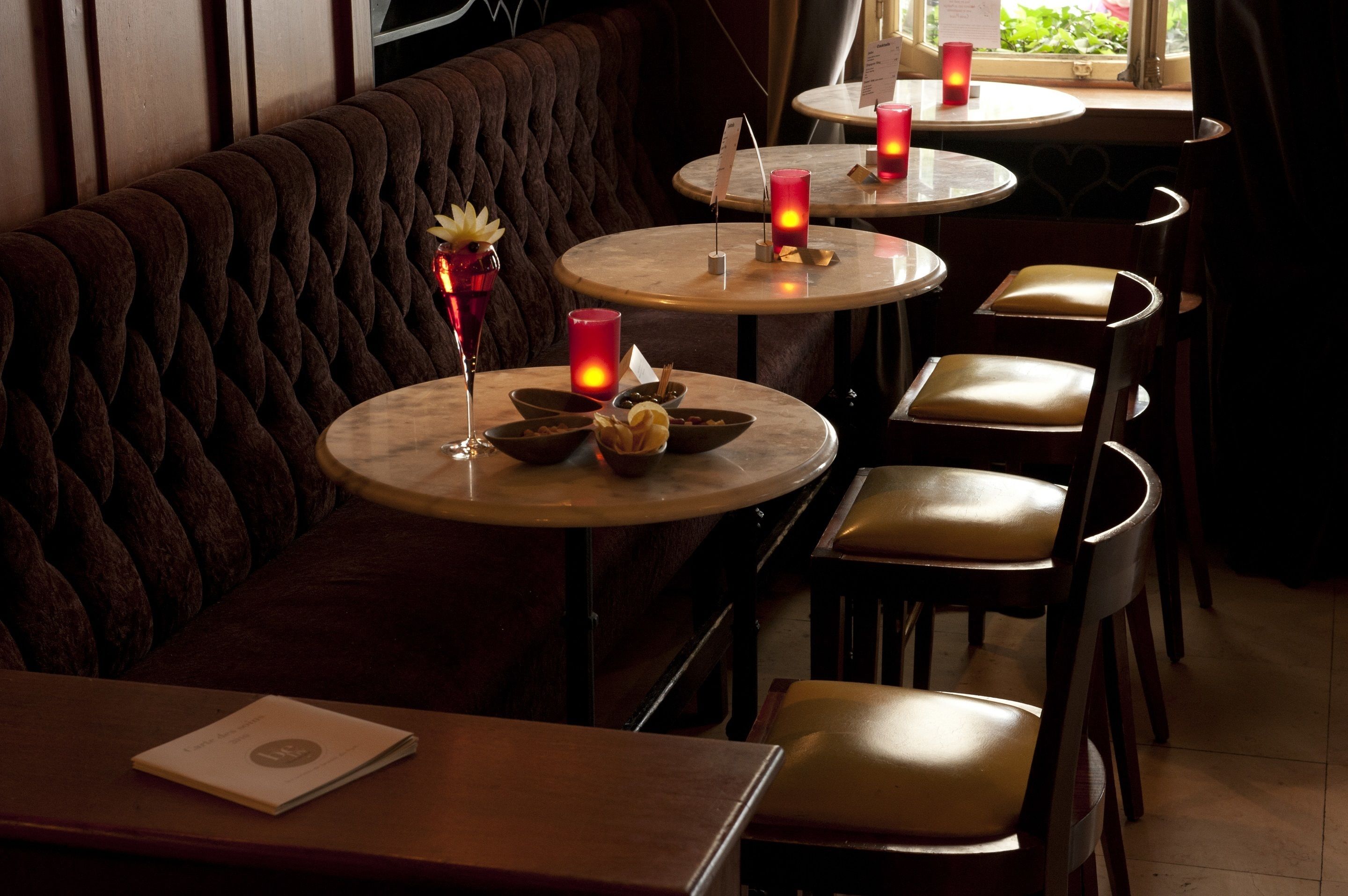 A restaurant with round tables, cushioned booths, and candles.