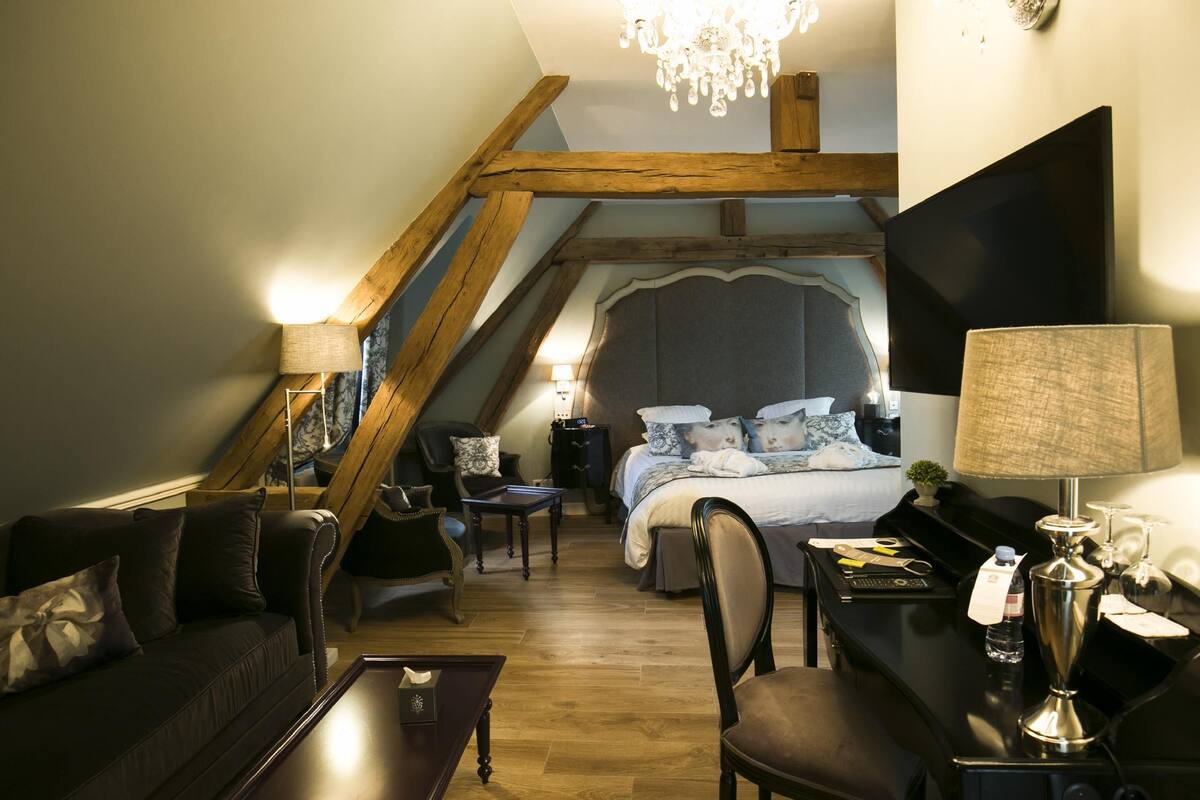 Quarto de hotel acolhedor com cama, escrivaninha, poltrona, sofá e candelabro.