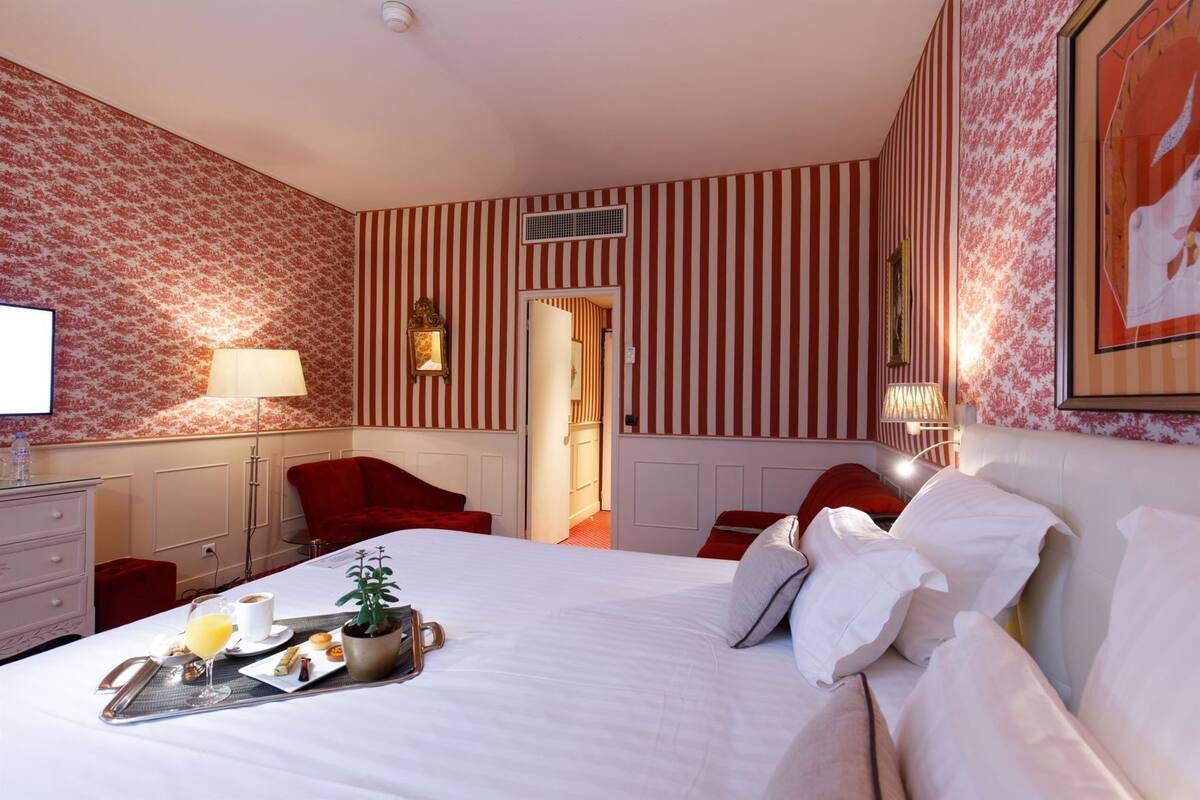 Quarto de hotel com cama, escrivaninha com abajur, cadeira e bandeja de café da manhã sobre a cama.