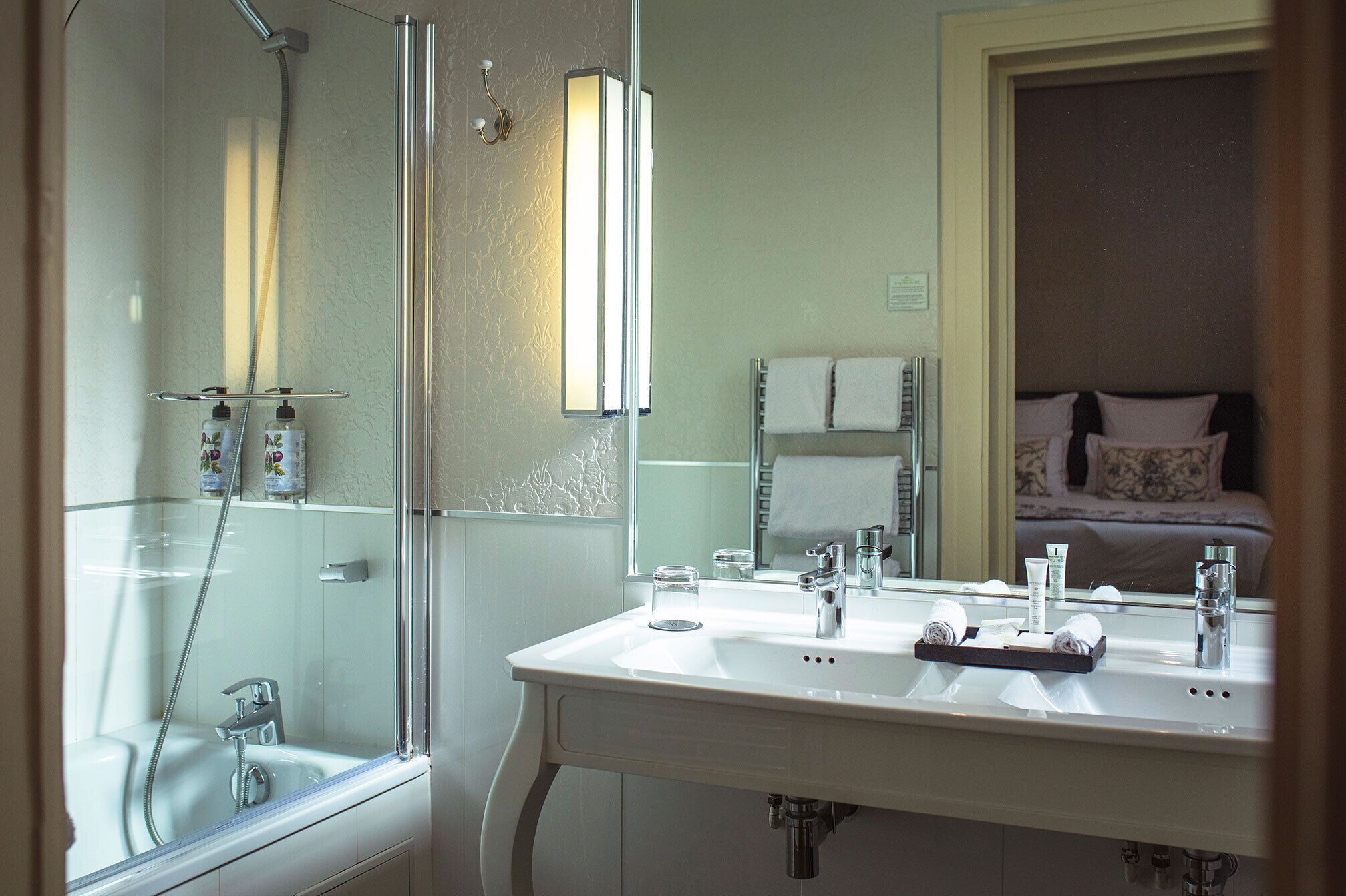 A bathroom with a glass-enclosed shower, a white sink with two mirrors, and a visible towel rack.