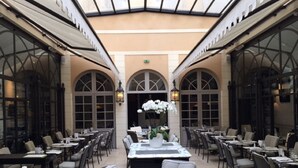 A spacious indoor dining area with high ceilings and large windows, featuring tables and chairs arranged for dining.