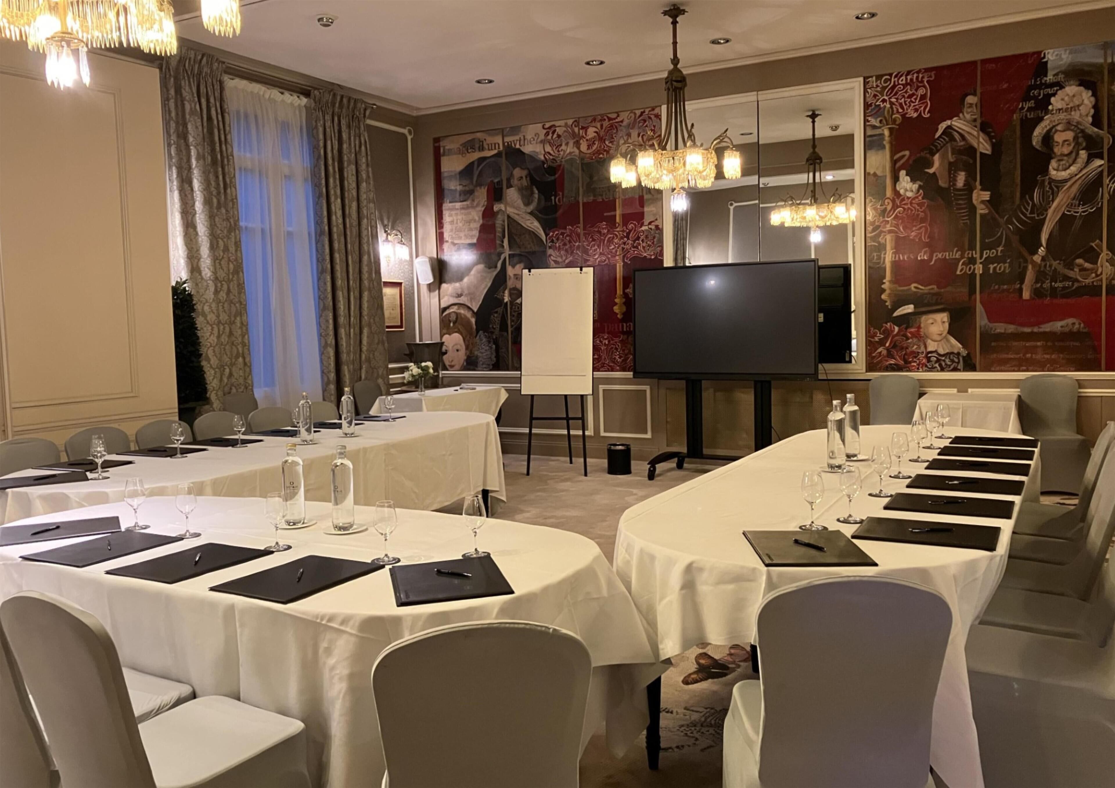 Un salón de conferencias con mesas redondas, sillas, una pantalla grande y decoración en las paredes.