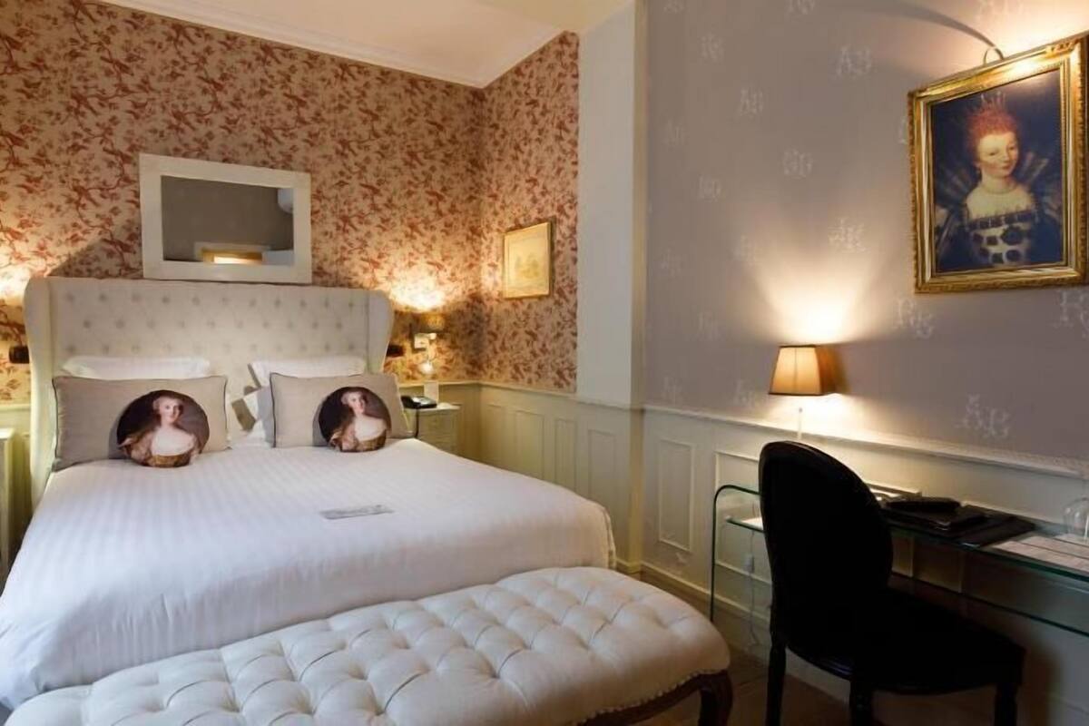 Quarto de hotel com cama, mesas de cabeceira, escrivaninha e uma cadeira.
