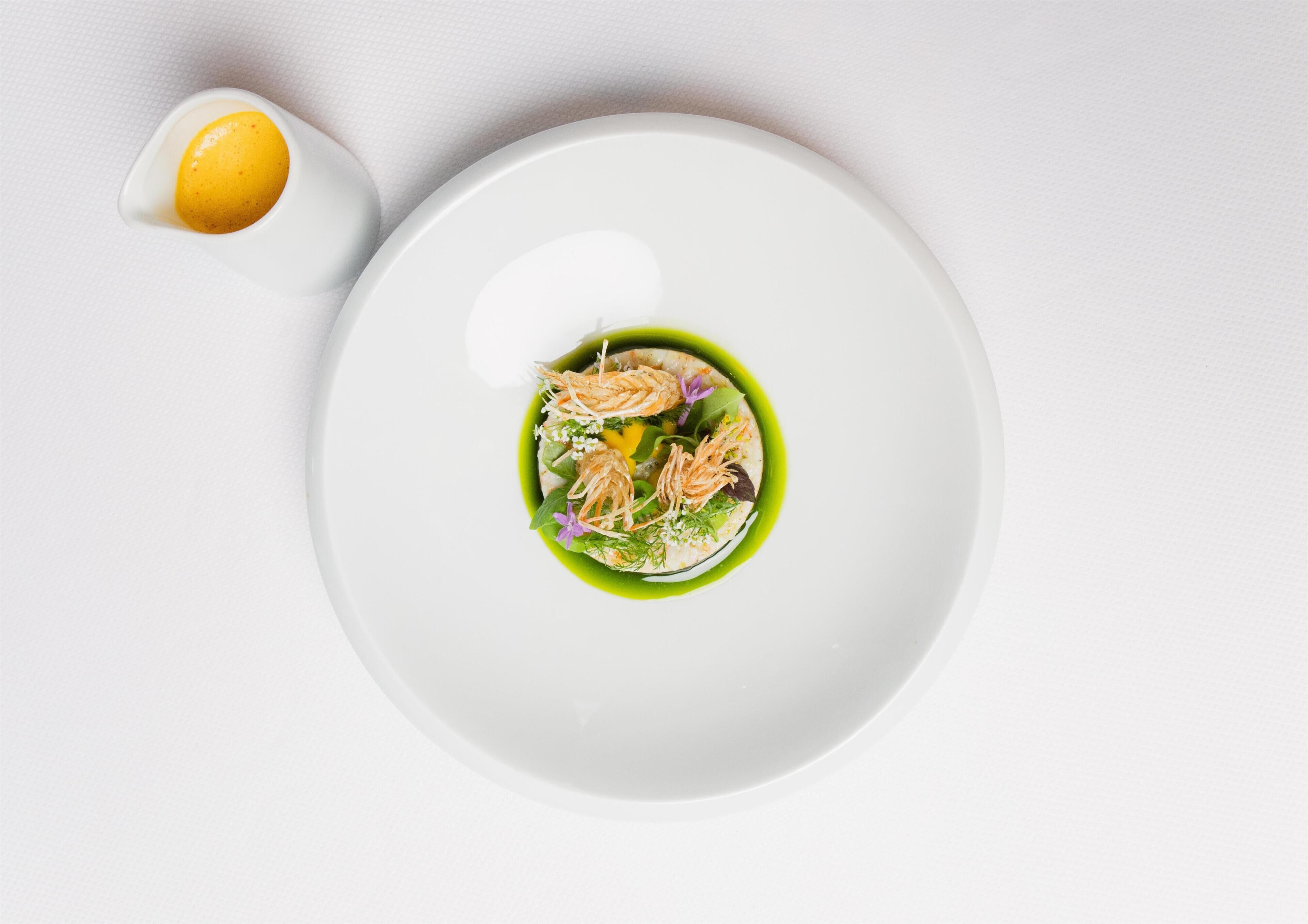 A white plate with a green sauce and seafood garnish.
