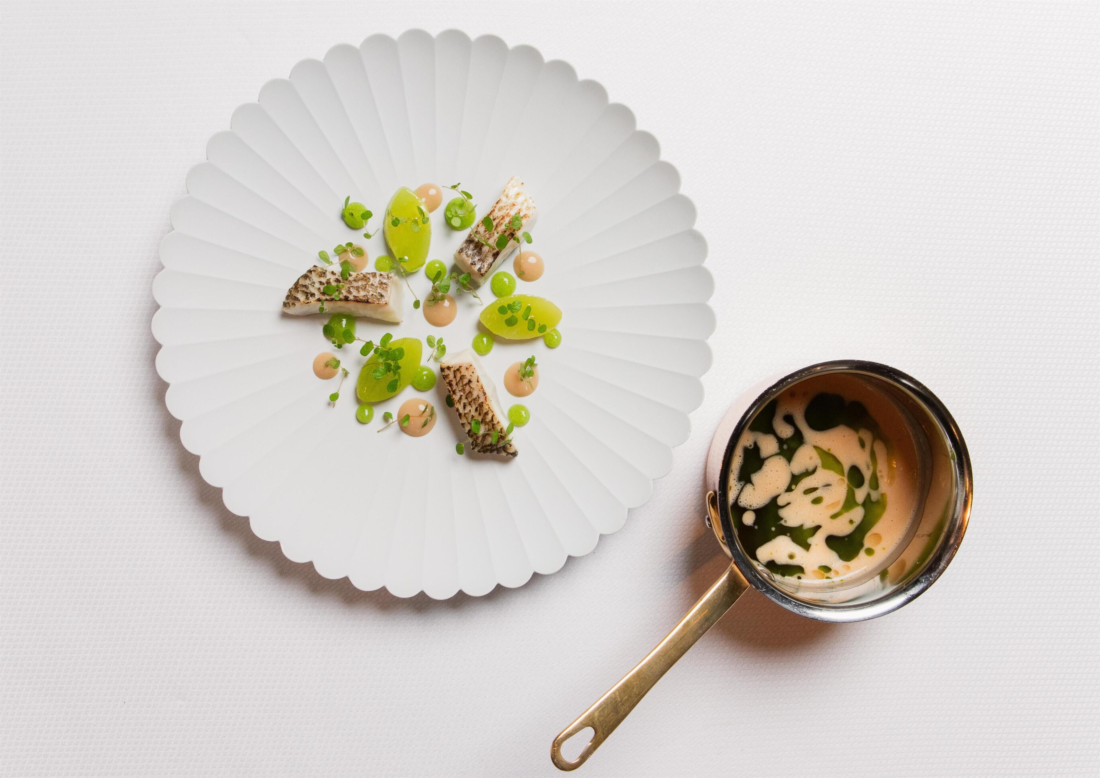 A white plate with food and a small cup of sauce on a white surface.