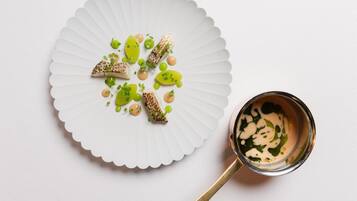 A white plate with food and a small cup of sauce on a white surface.