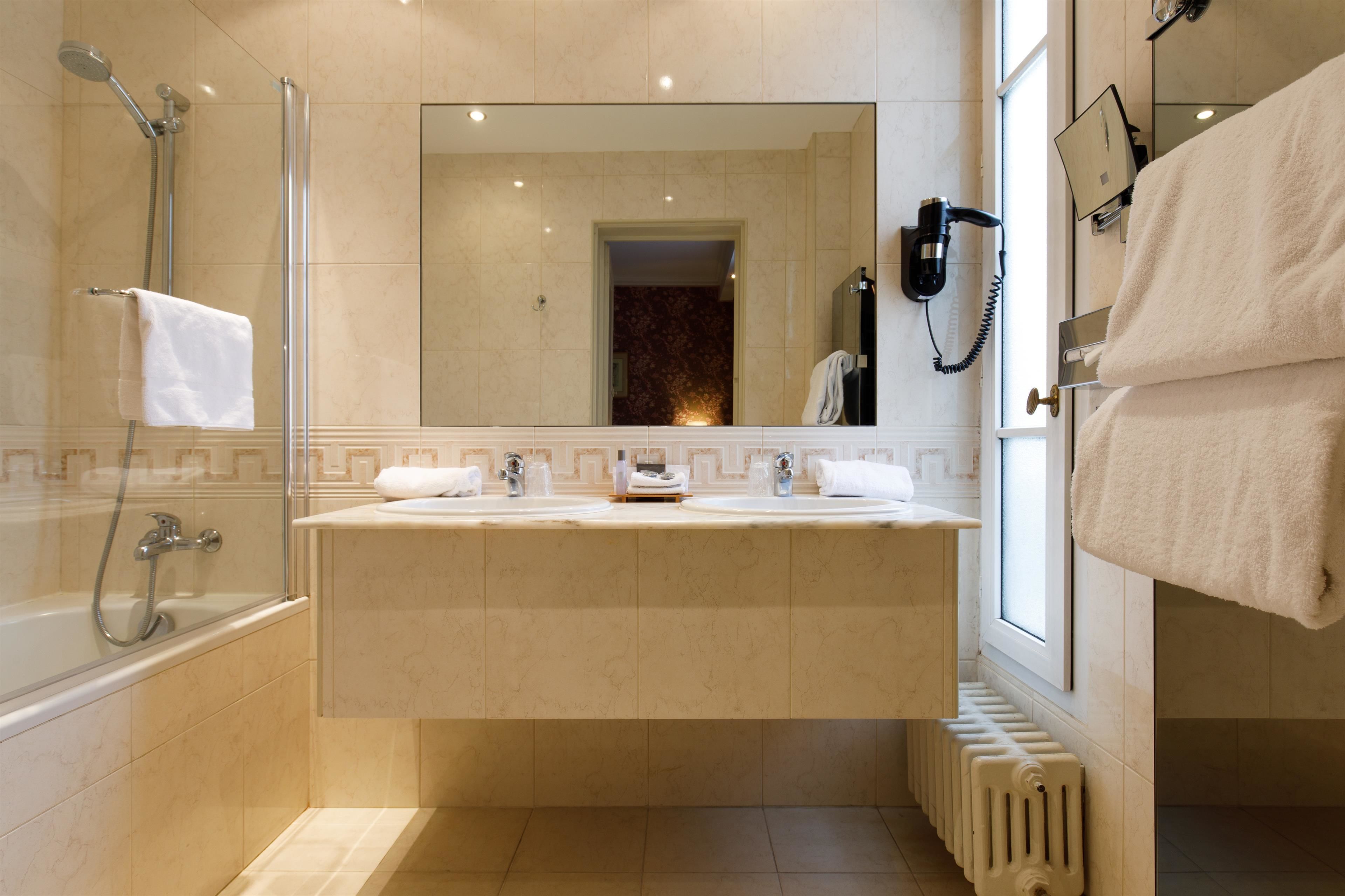 Ein Badezimmer mit einer Badewanne, zwei Waschbecken, einem Spiegel, einem Haartrockner und einem Handtuchhalter.