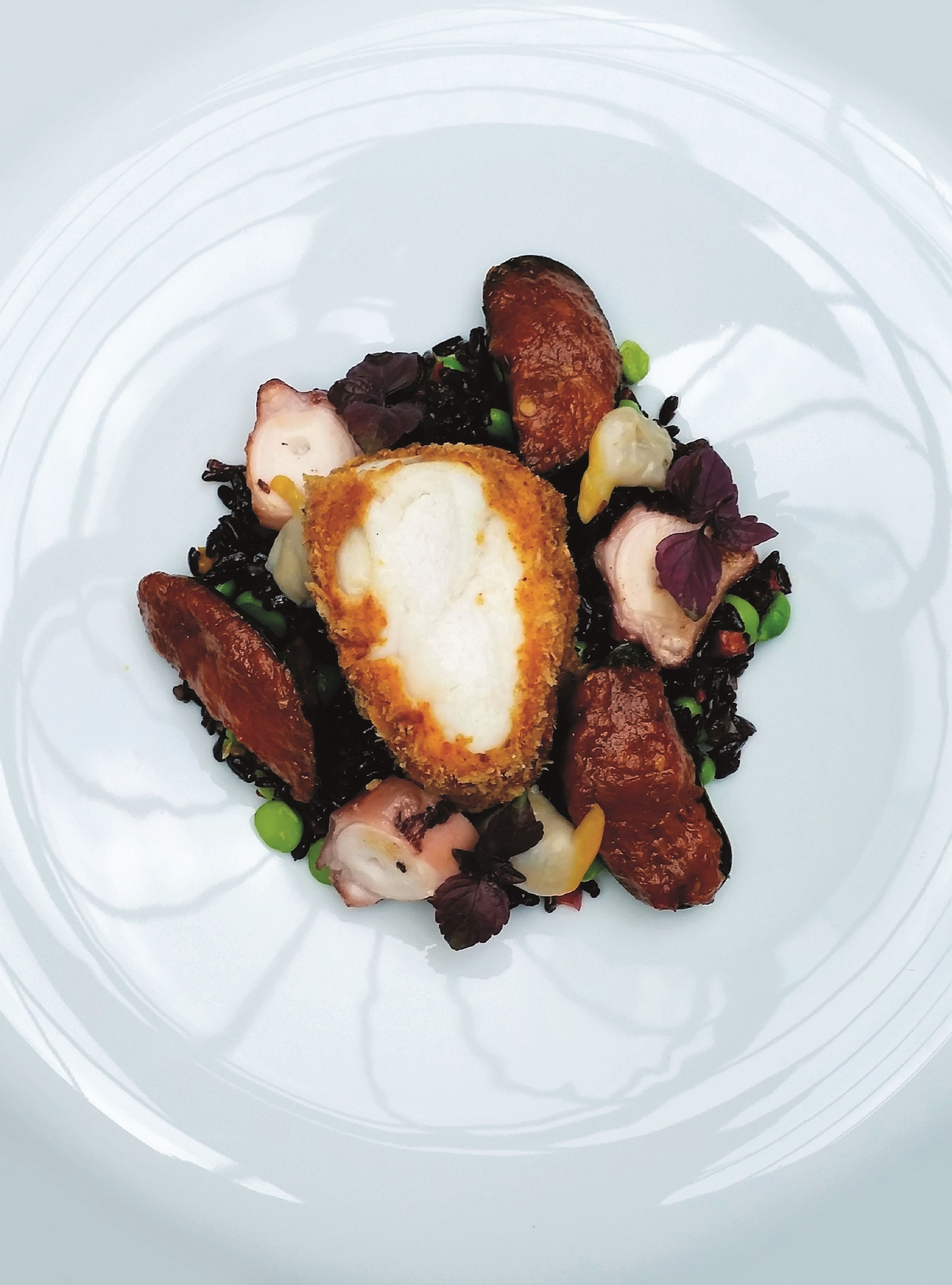 A white plate with a piece of breaded chicken breast, peas, and a mix of vegetables.