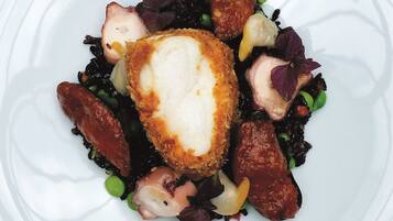A white plate with a piece of breaded chicken breast, peas, and a mix of vegetables.