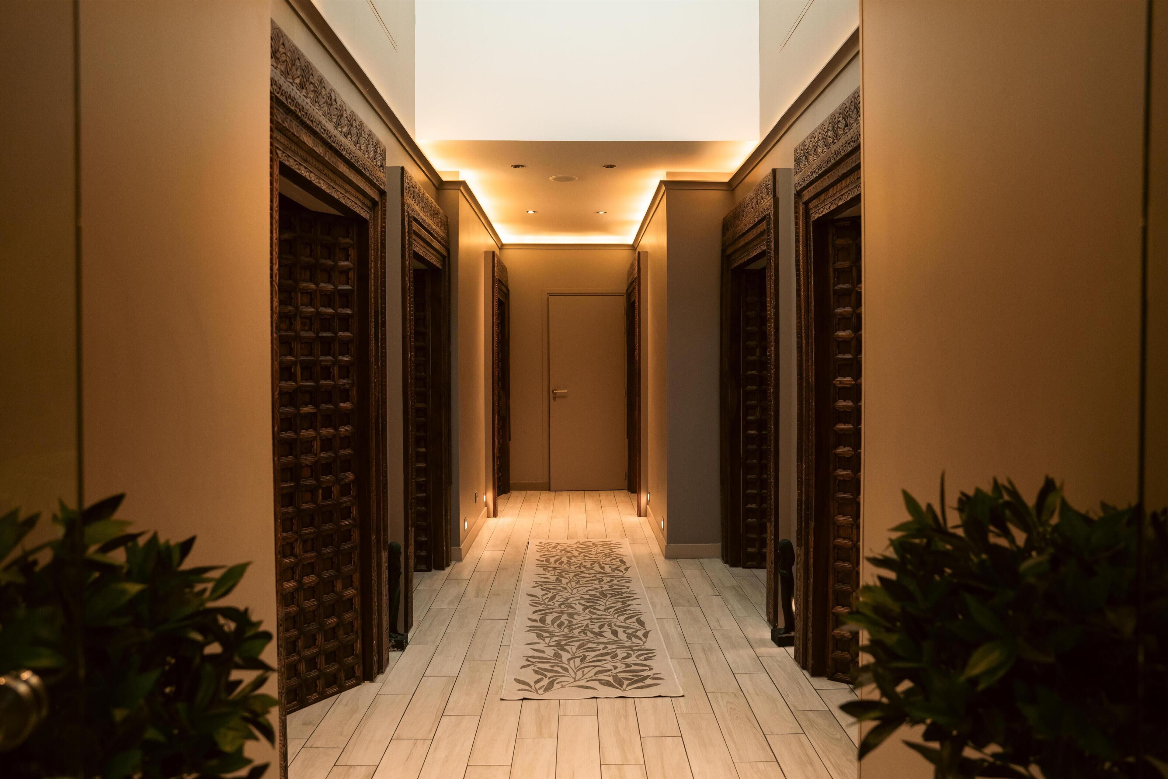 A hallway with a patterned rug, wooden doors, and a light source above.