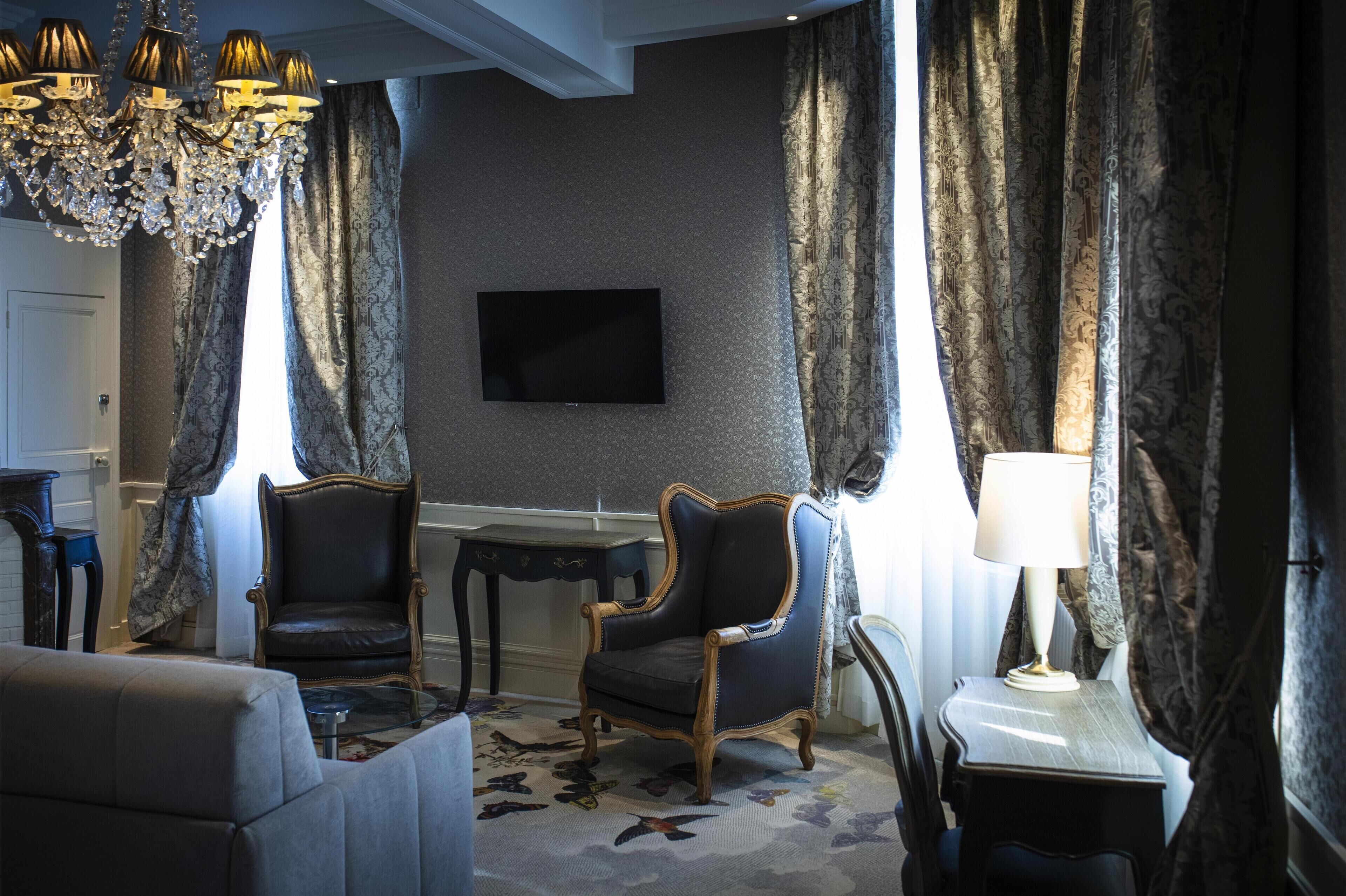 A room with a chandelier, two armchairs, a television, and a table with a lamp.