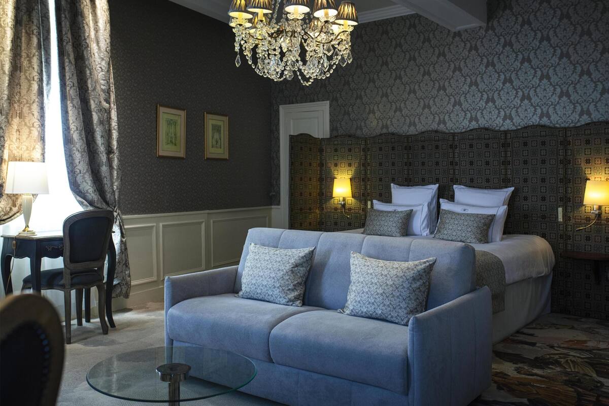Quarto com cama grande, sofá, lustre e papel de parede estampado.