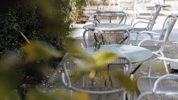 Outdoor seating with round tables and white chairs, surrounded by greenery.