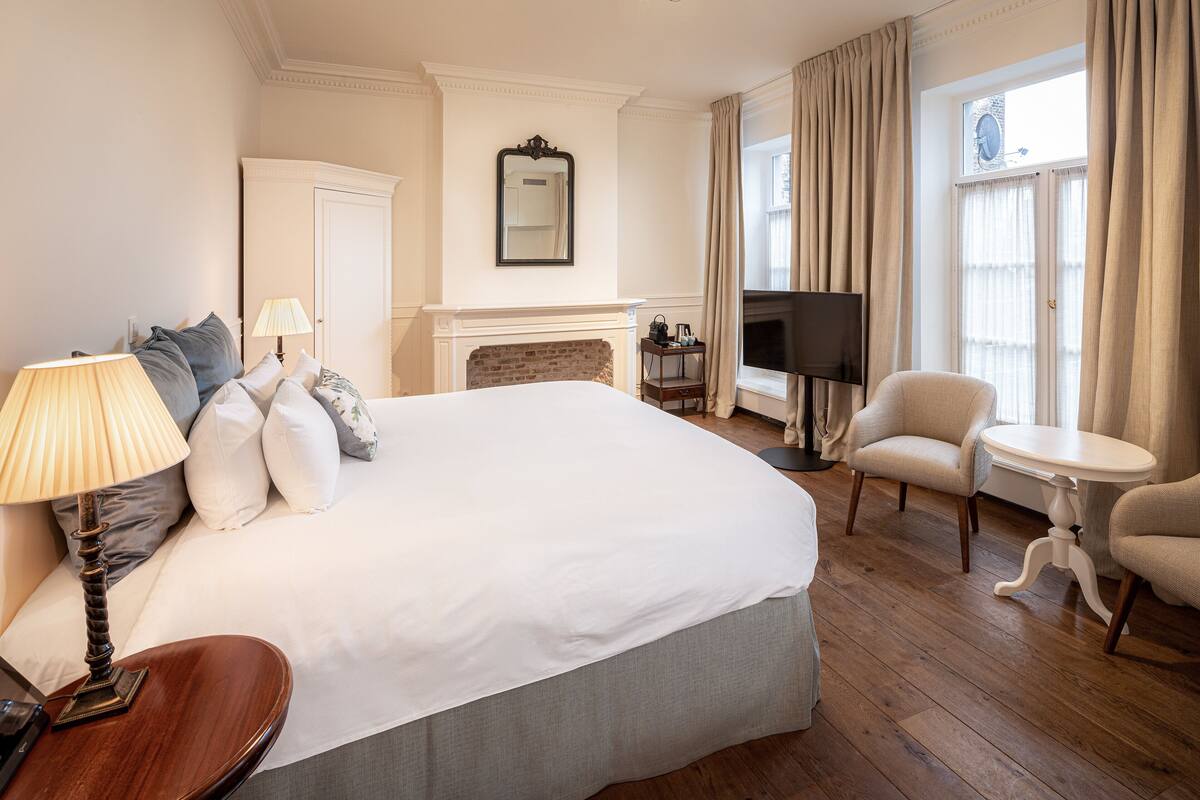 A hotel room with a large bed, a TV, a fireplace, a chair, and a table.