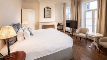 A hotel room with a large bed, a TV, a fireplace, a chair, and a table.