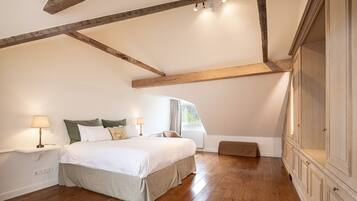 Une chambre avec un plafond en bois, un grand lit, une table de chevet avec une lampe, un banc et une armoire.