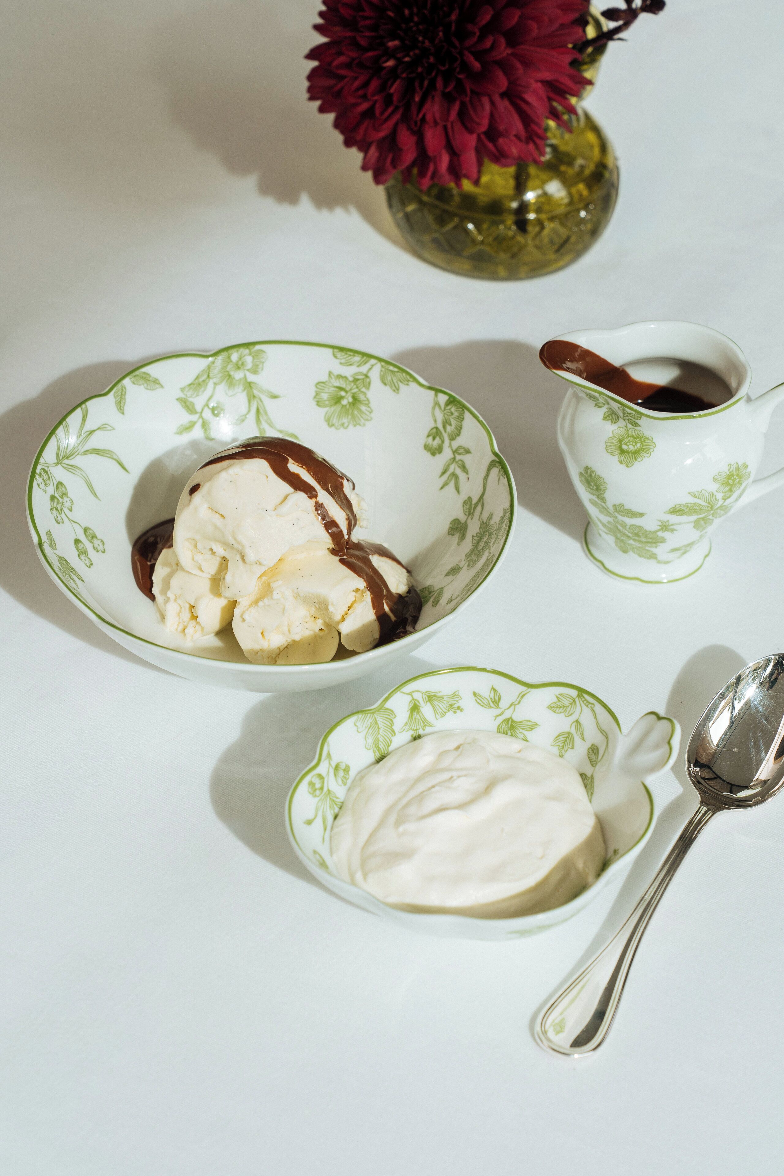 Una mesa con un tazón de helado y una taza pequeña de salsa de chocolate.