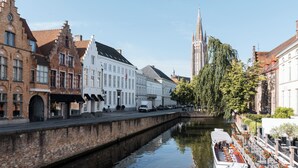 Un canal con un barco amarrado a la derecha, bordeado por edificios históricos y una torre de iglesia al fondo.