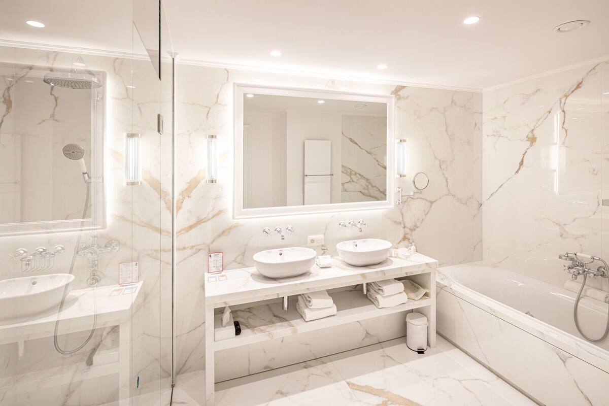 A modern bathroom with a glass-enclosed shower, two sinks, a large mirror, and a bathtub.
