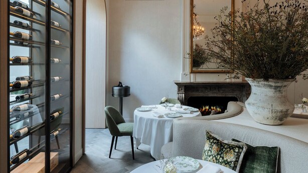 Un comedor con mesas redondas dispuestas para una comida, una vinoteca, una chimenea y un candelabro.