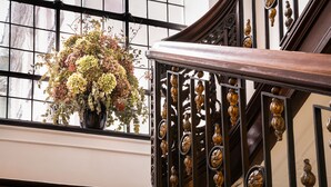 Una escalera con barandales ornamentales y un arreglo floral en el descansillo.