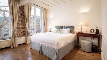 A bedroom with a large bed, a wooden floor, a brick wall, and a window with curtains.