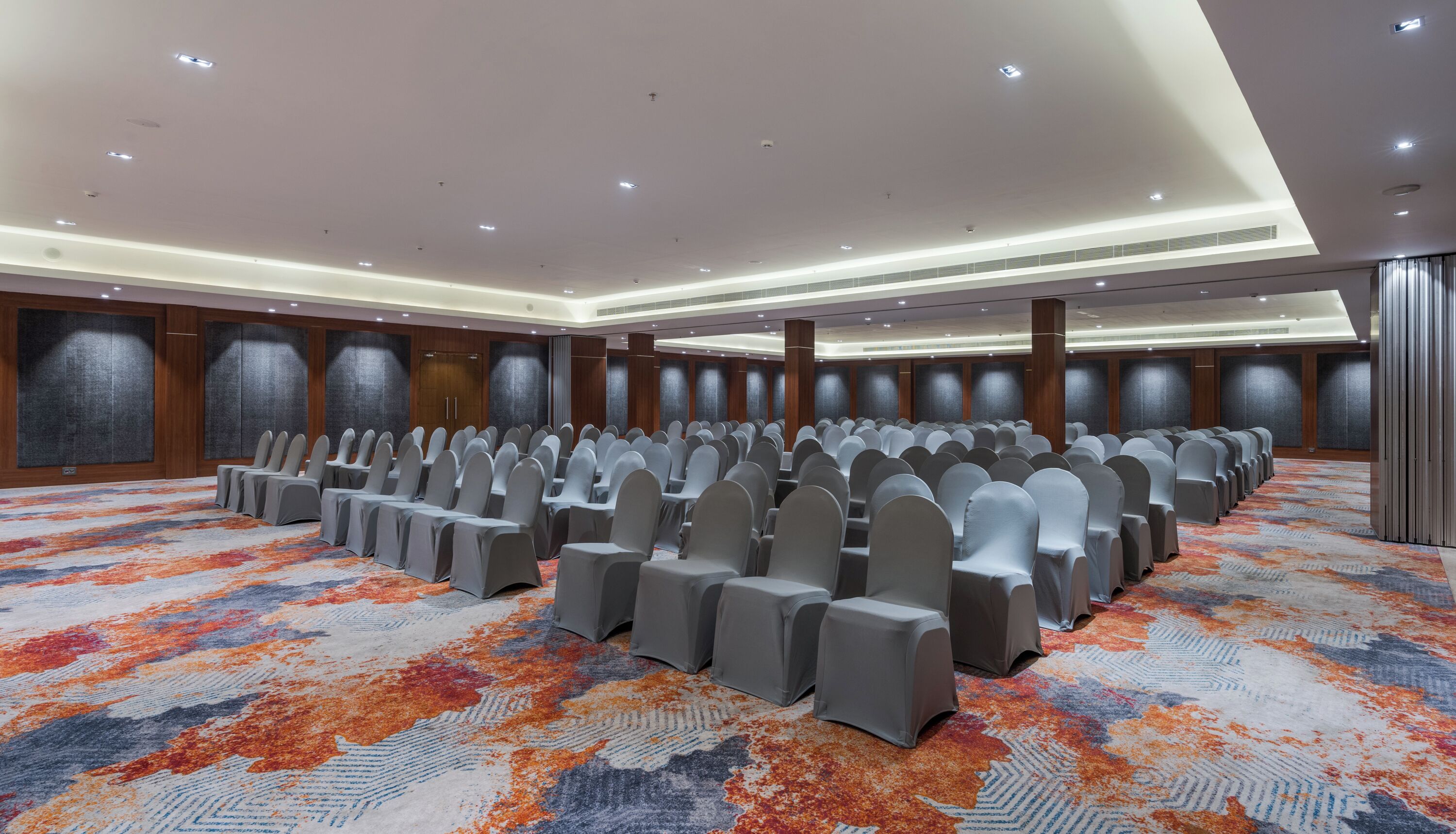 A conference room with rows of chairs and tables, a patterned carpet, and a high ceiling with recessed lighting.