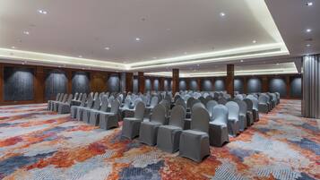 A conference room with rows of chairs and tables, a patterned carpet, and a high ceiling with recessed lighting.