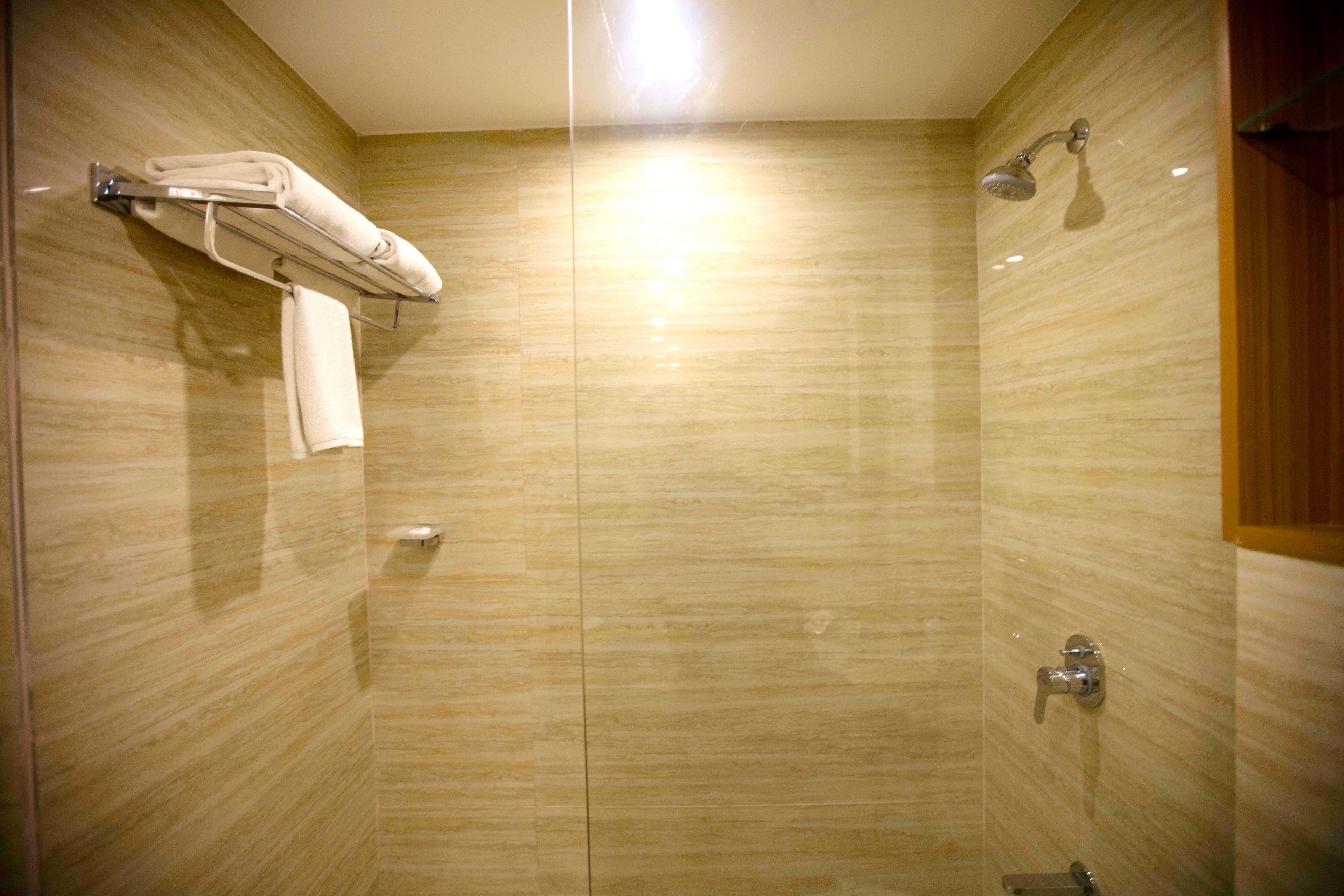 A bathroom with a glass partition, a towel rack, a showerhead, and a toilet.