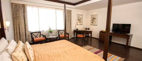 A hotel room with a large bed, a desk, a TV, and a window with curtains.