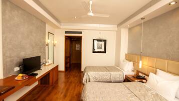 A hotel room with two beds, a television on a wooden console, a ceiling fan, and a framed picture on the wall.