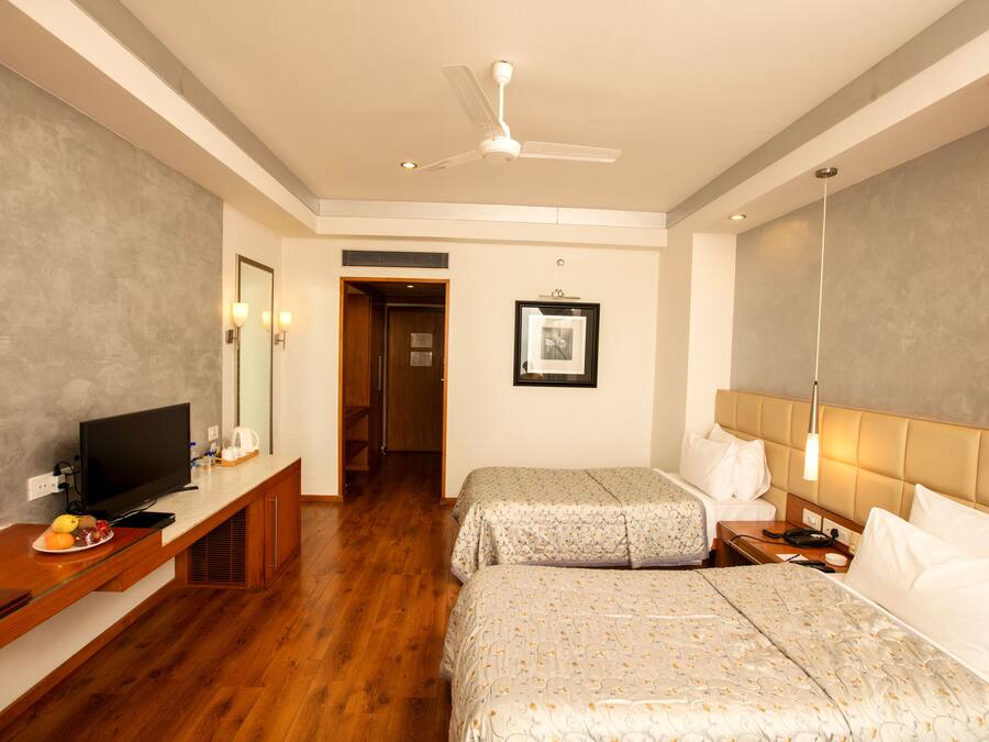 A hotel room with two beds, a television on a wooden console, a ceiling fan, and a framed picture on the wall.