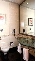 Un baño con lavamanos de vidrio, inodoro, espejo y teléfono.