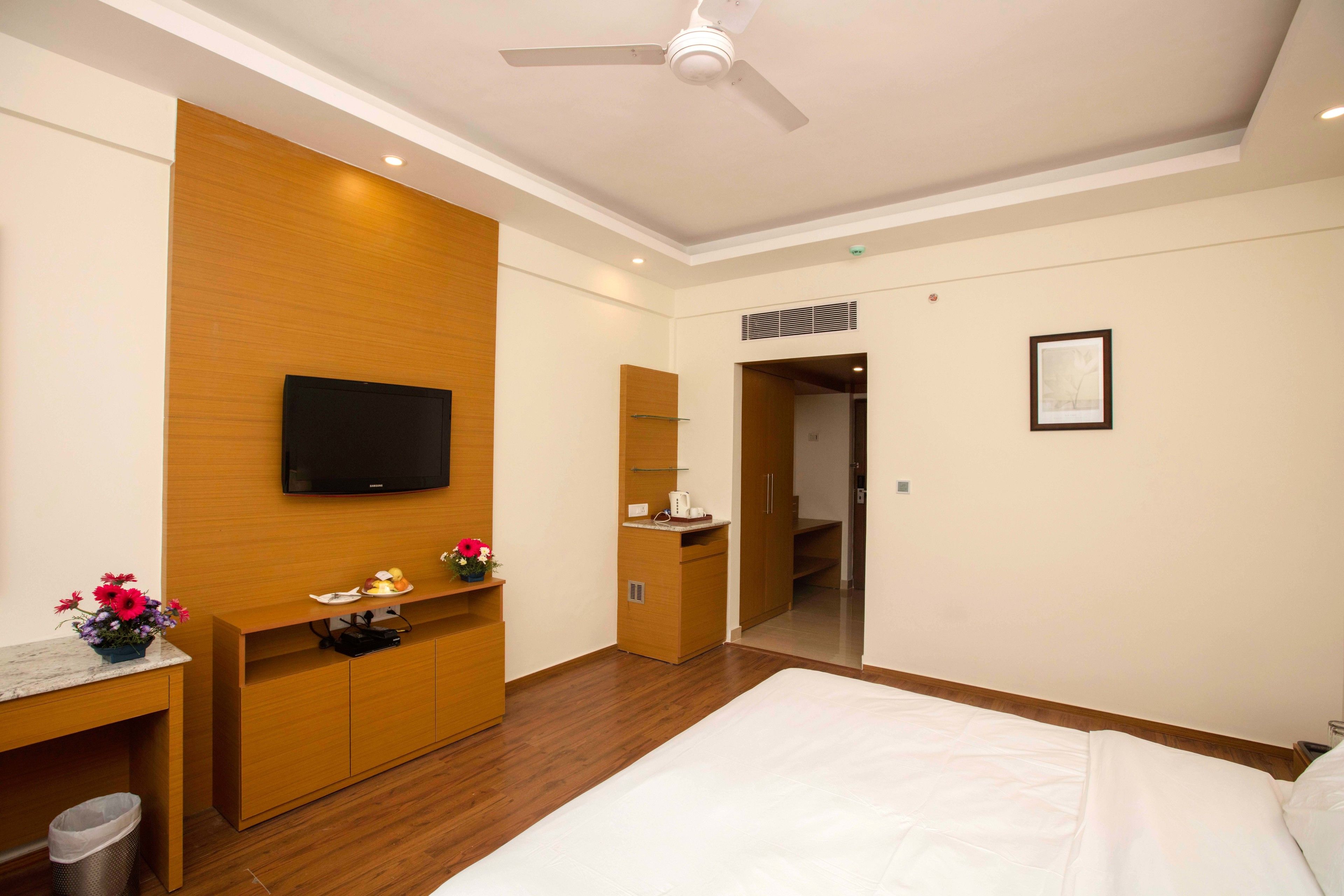 A hotel room with a bed, a desk, a TV, a wardrobe, a mirror, and a door leading to a bathroom.
