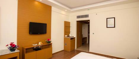 A hotel room with a bed, a desk, a TV, a wardrobe, a mirror, and a door leading to a bathroom.