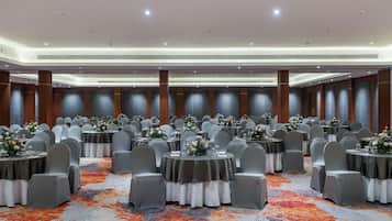 A large banquet hall with round tables, grey chairs, and floral centerpieces.