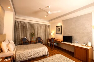 Habitación de hotel con una cama, dos sillas, un escritorio con televisor, una lámpara y una cafetera.