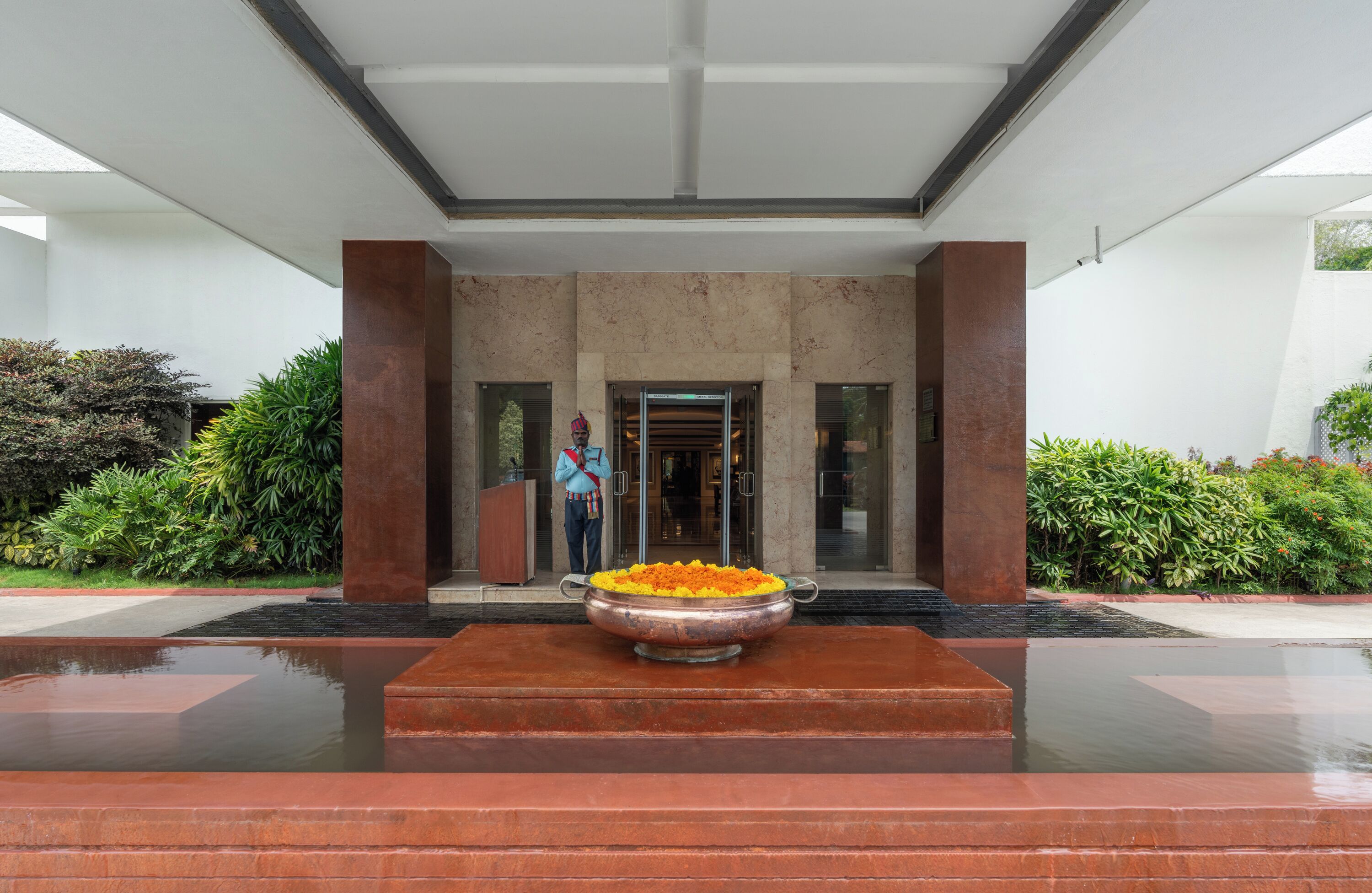 Ein moderner Hauseingang mit einer großen Metallschale, gefüllt mit orangefarbenen Blumen, umgeben von einem Wasserspiel.