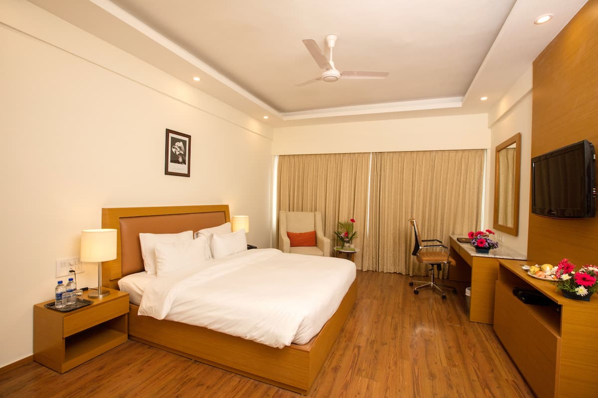 A hotel room with a bed, a desk, a chair, a television, and a ceiling fan.