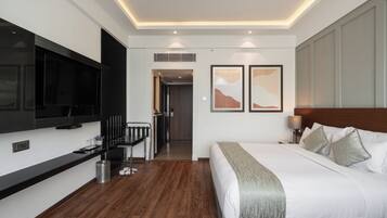A modern hotel room with a large bed, a flat-screen TV mounted on the wall, a desk with a chair, and a small trash can.